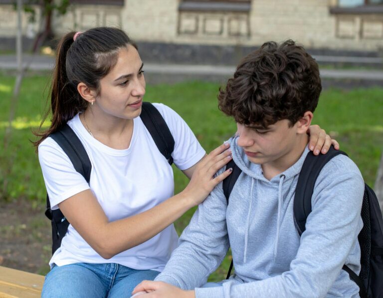 A teenage girl comforts a sad male friend outdoors, providing support and empathy.