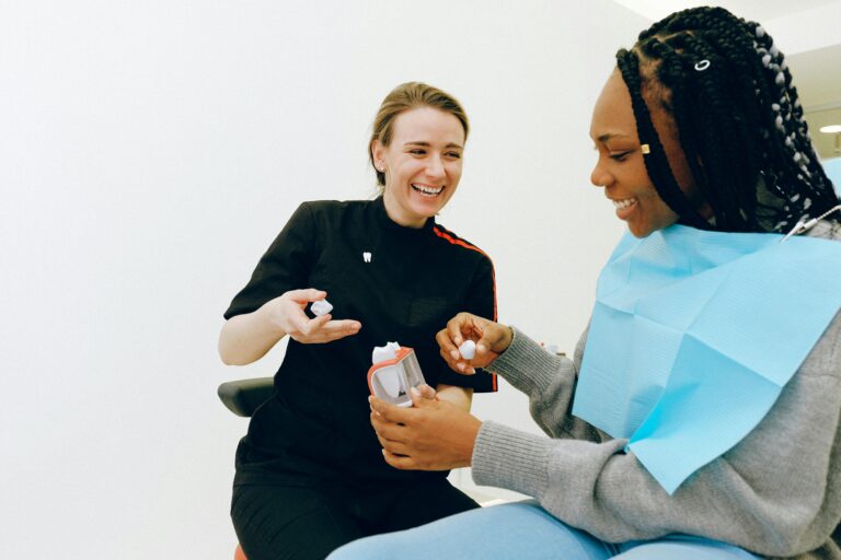 A dentist demonstrates dental care to a smiling patient in a clinic setting.